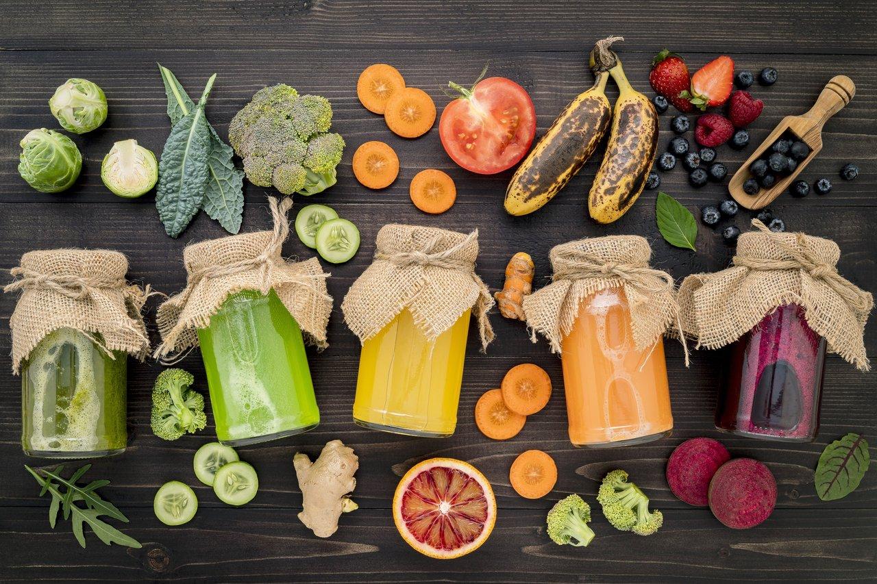 Jars de detox juice colorés avec fruits et légumes frais sur une table en bois, parfaits pour une alimentation équilibrée.