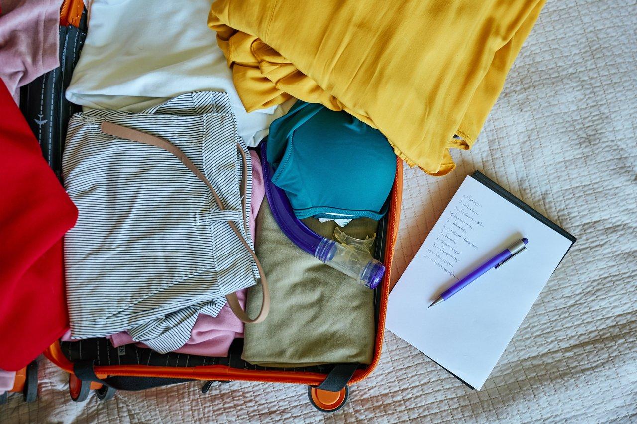 Valise bien organisée avec une checklist écrite, documents de voyage et vêtements prêts pour un voyage réussi.